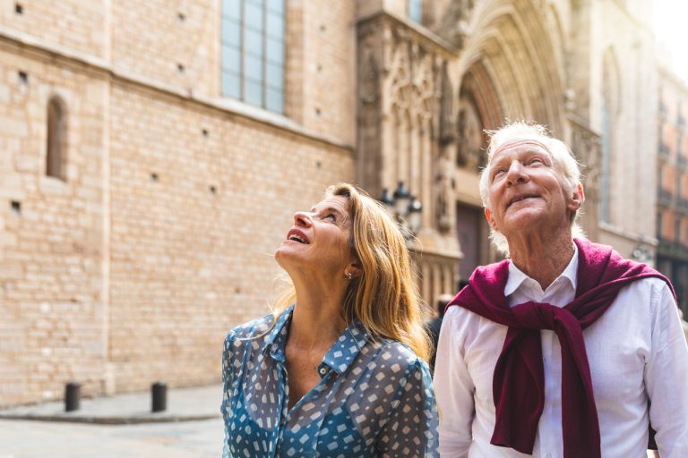 Senior couple of tourists visiting the old town in Barcelona. Adult woman and man looking up at some beautiful architecture on a sunny day in Spain. Travel and tourism concepts